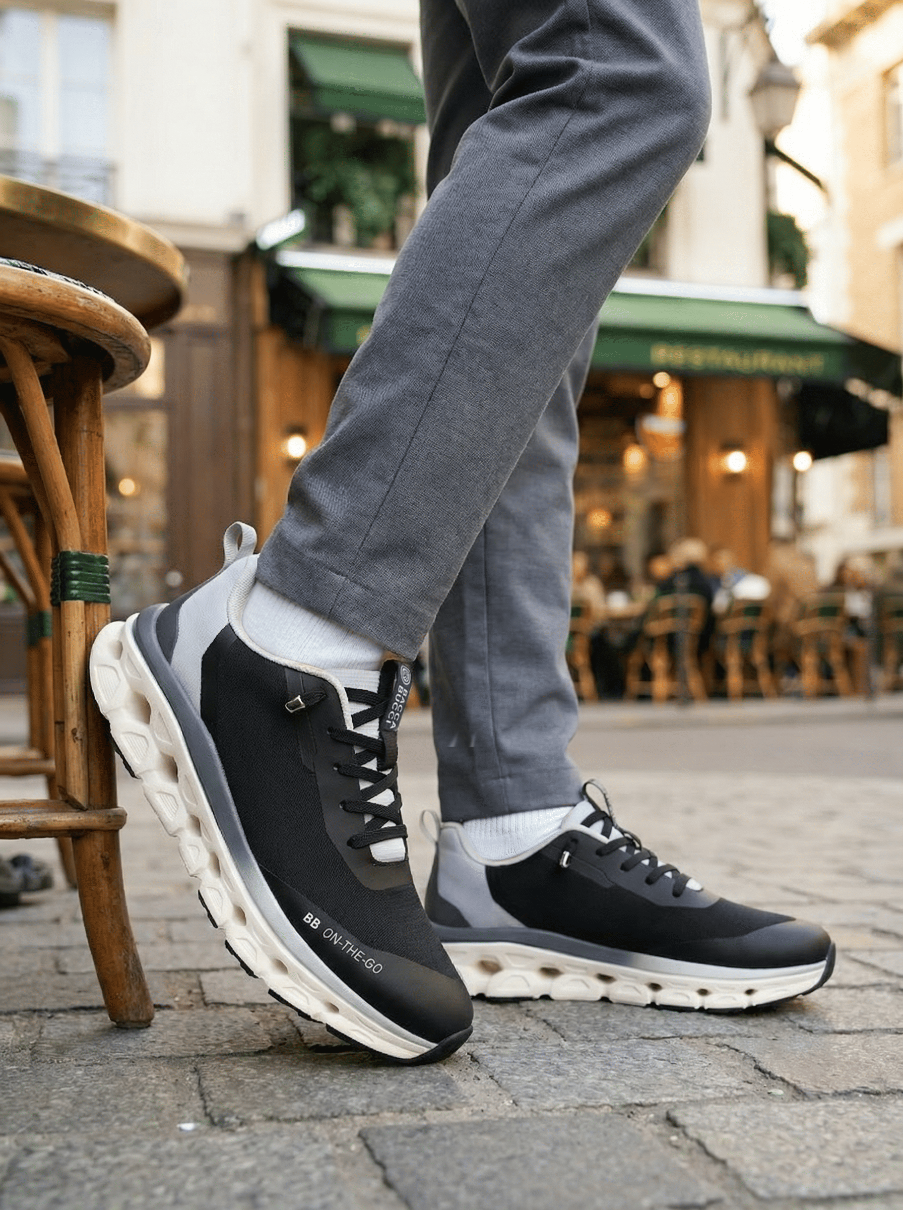 Person wearing black and gray  bacca bucci sneakers with a blurred street scene in the background.