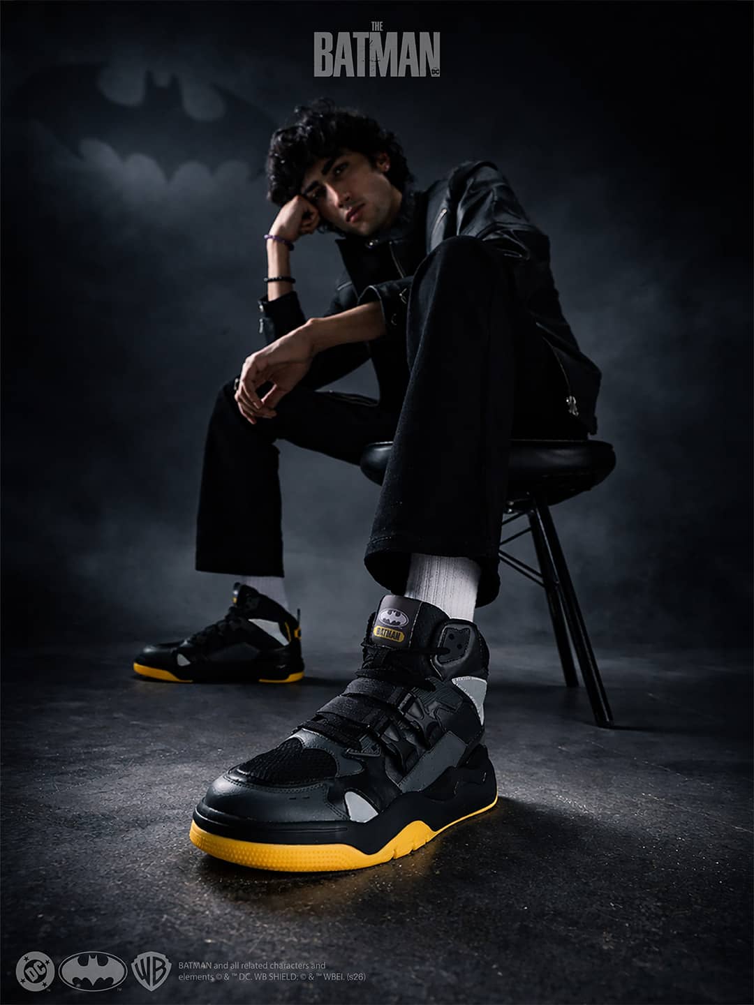 Person wearing black and yellow sneakers with a dark background and Batman logo.
