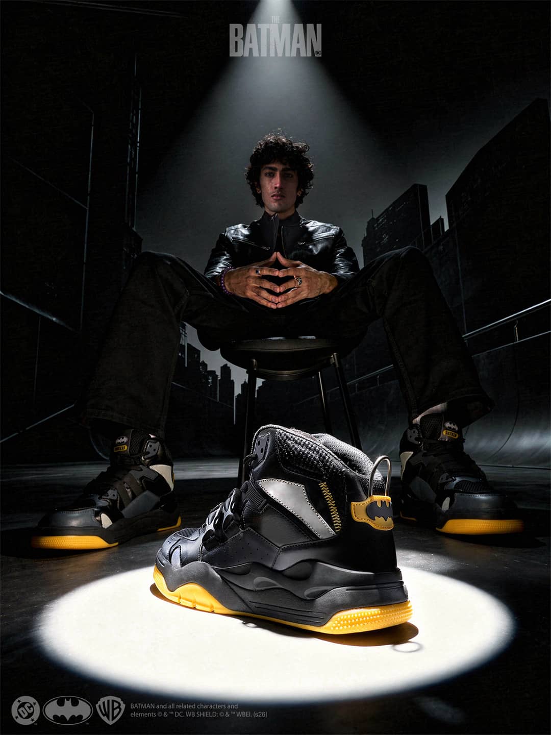 Person sitting on a ledge with a spotlight on black and yellow sneakers, Batman logo visible.