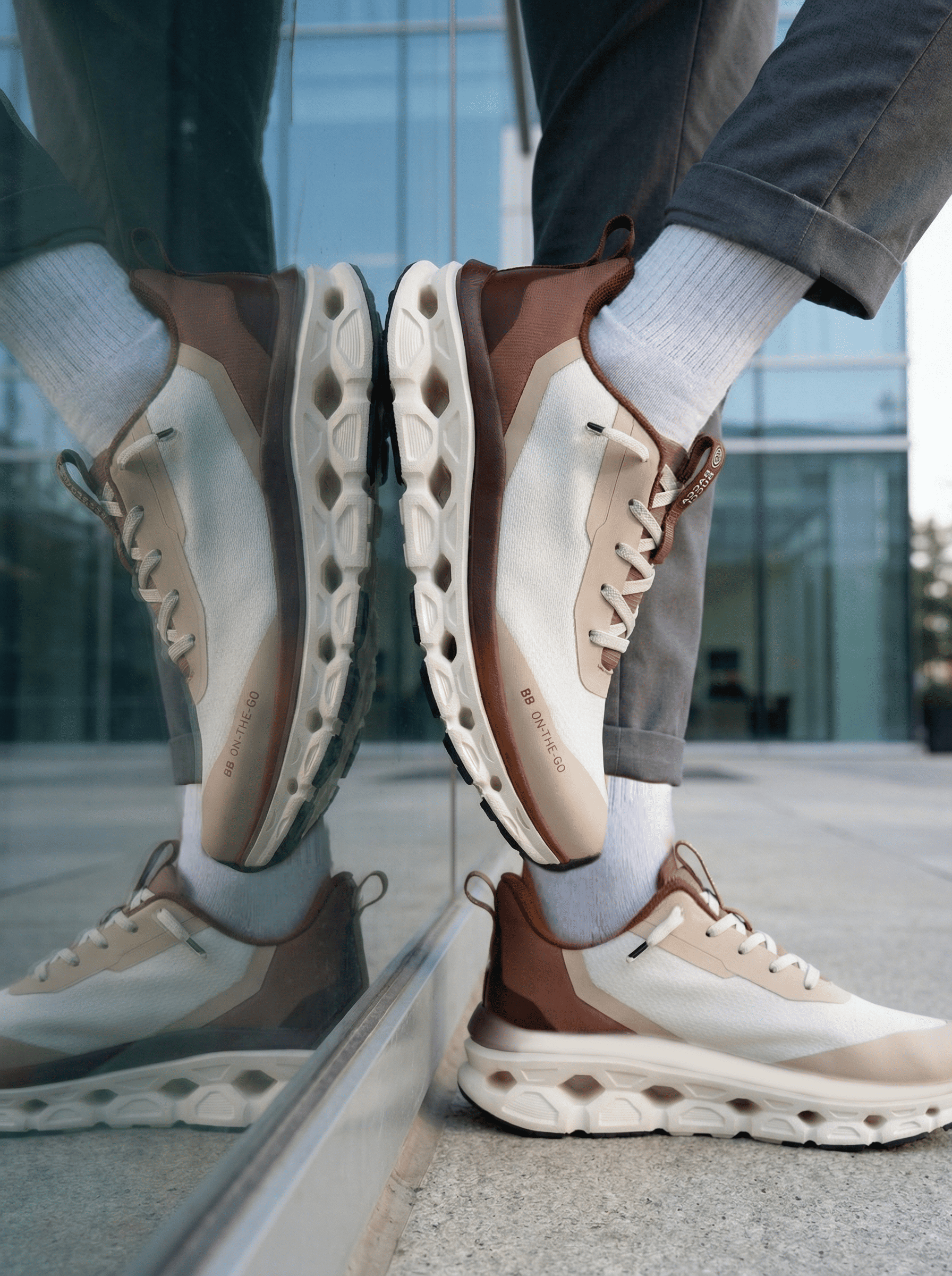 Person wearing brown and beige bacca bucci sneakers with a reflective surface in the background.