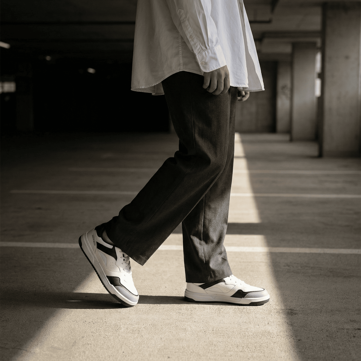 Person wearing bacca bucci  white sneakers with black stripes in a dimly lit parking garage.