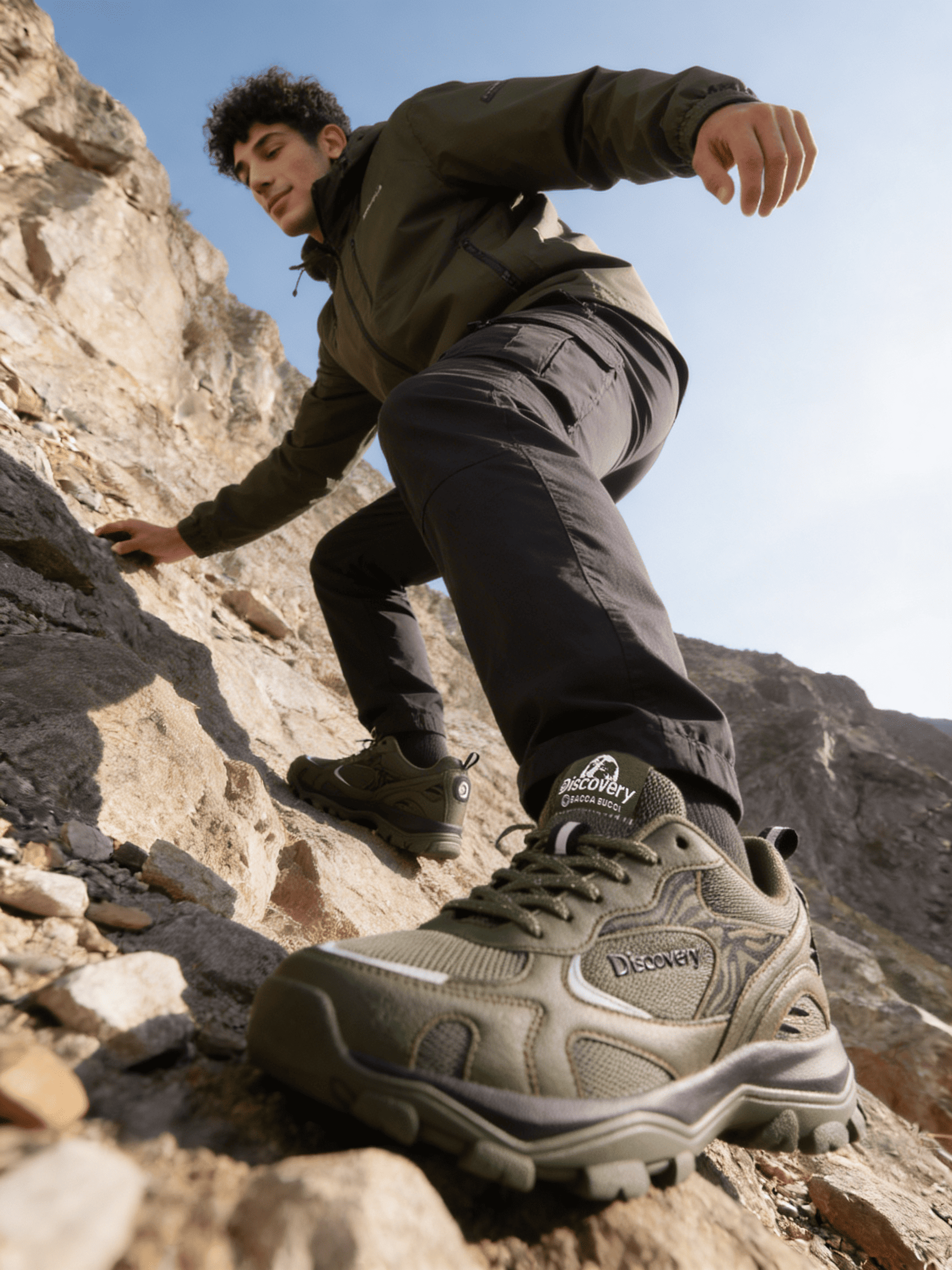 A person climbing a rocky mountain wearing hiking boots with 'discovery' branding.